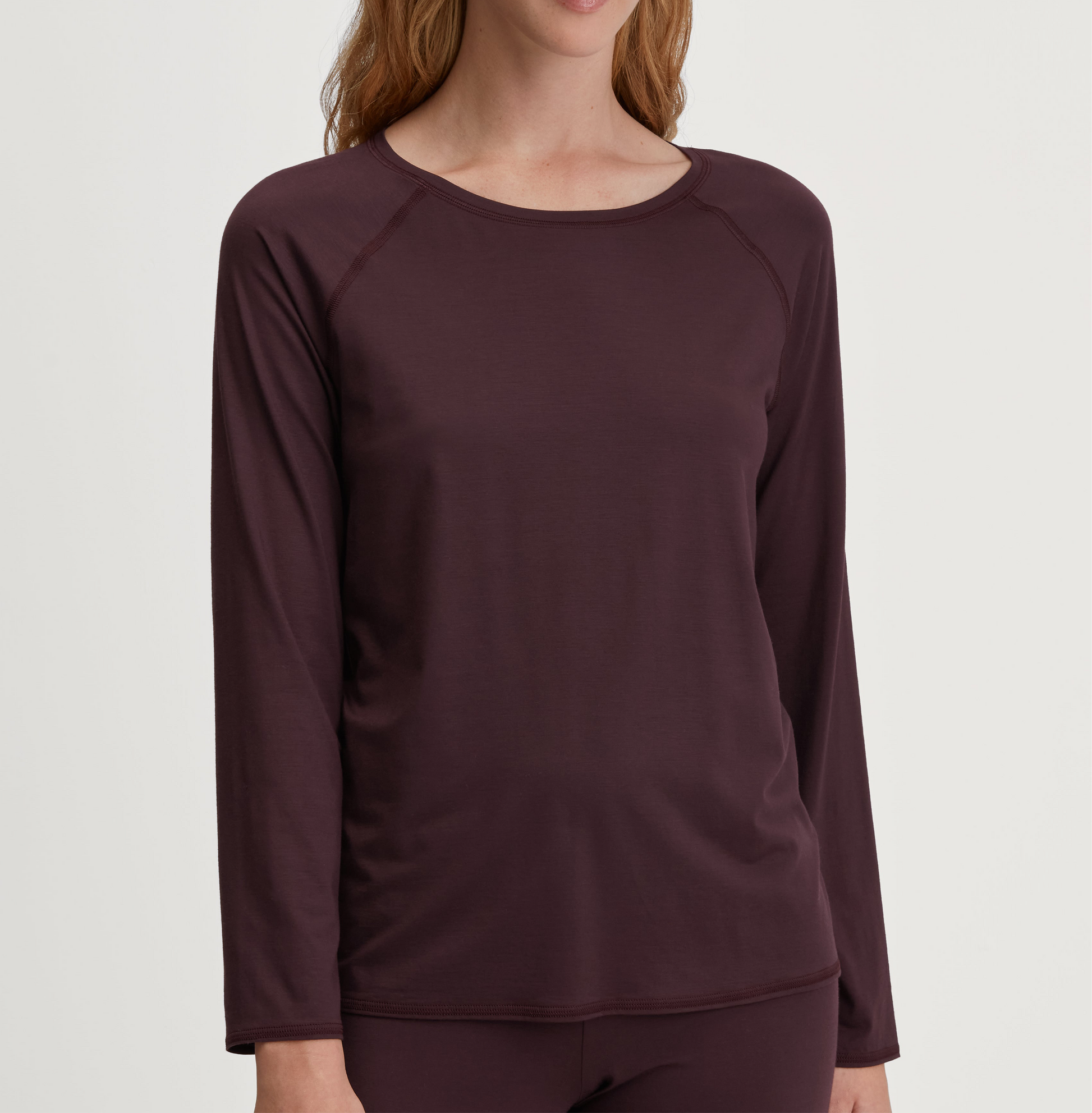 Maroon long-sleeve top worn by a person on a light gray background