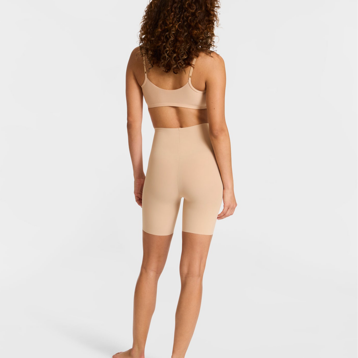 Woman wearing a beige sports bra and shorts set on a plain background