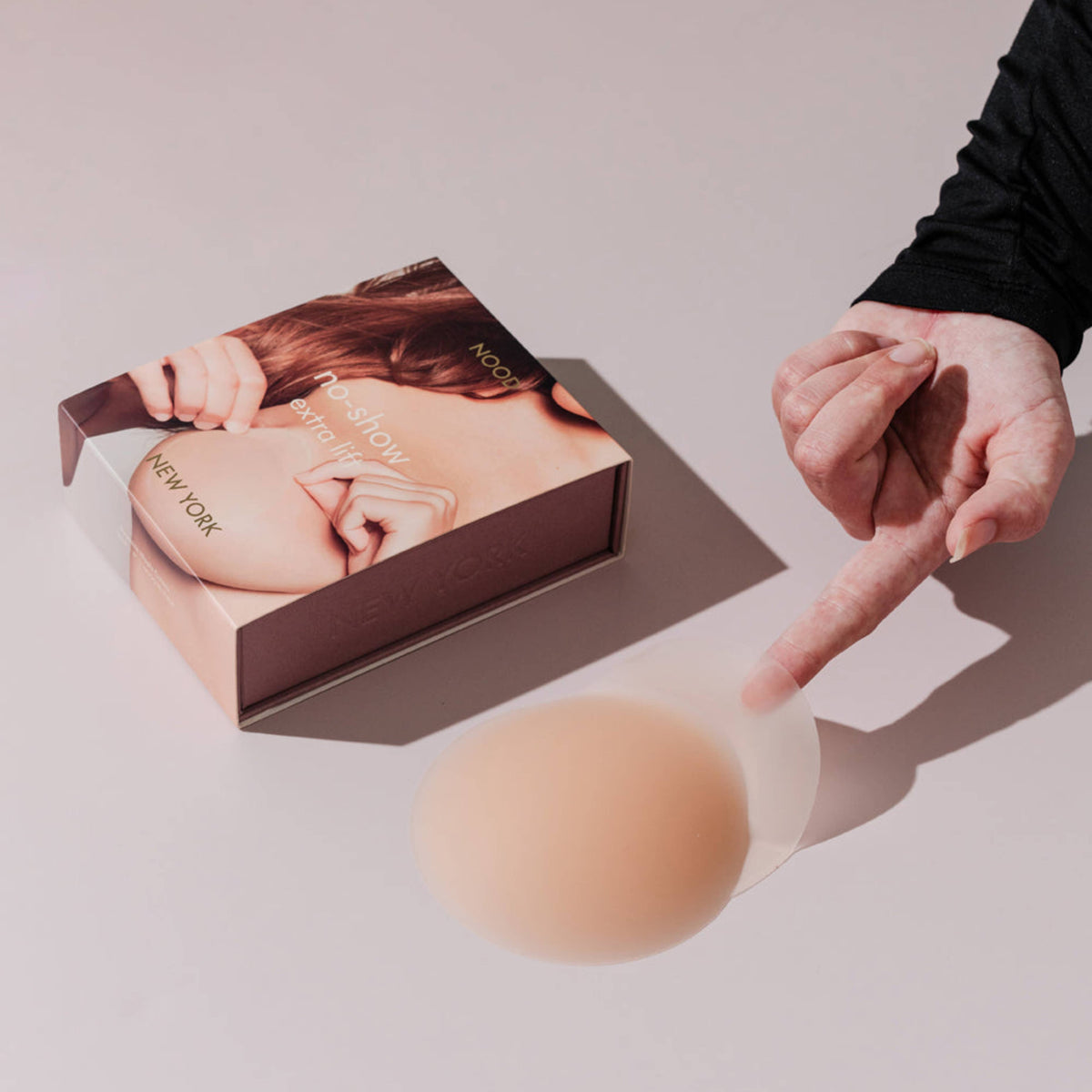 Person holding a beige silicone breast form next to its packaging on a light background