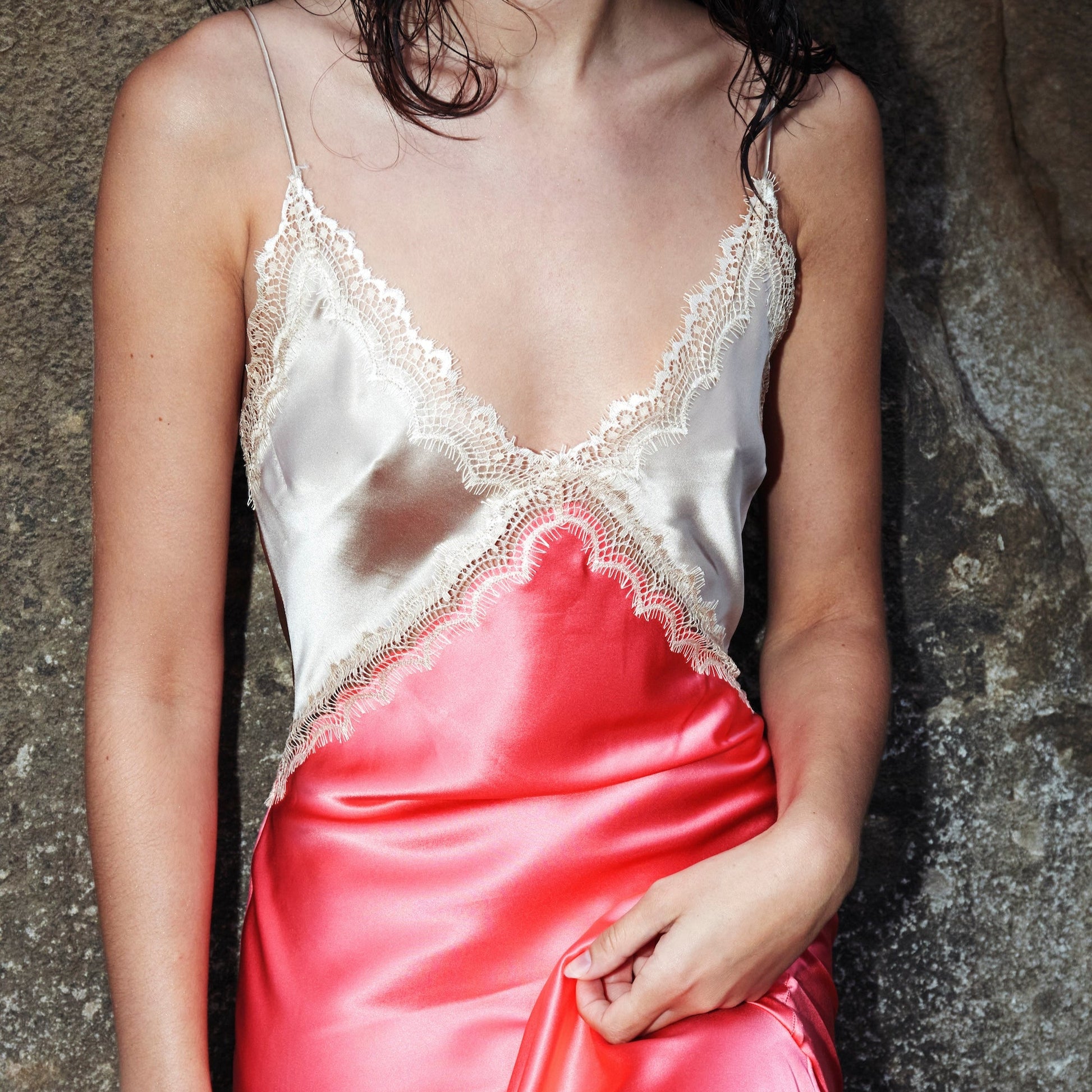 Person wearing a white lace top and pink satin skirt against a textured wall.