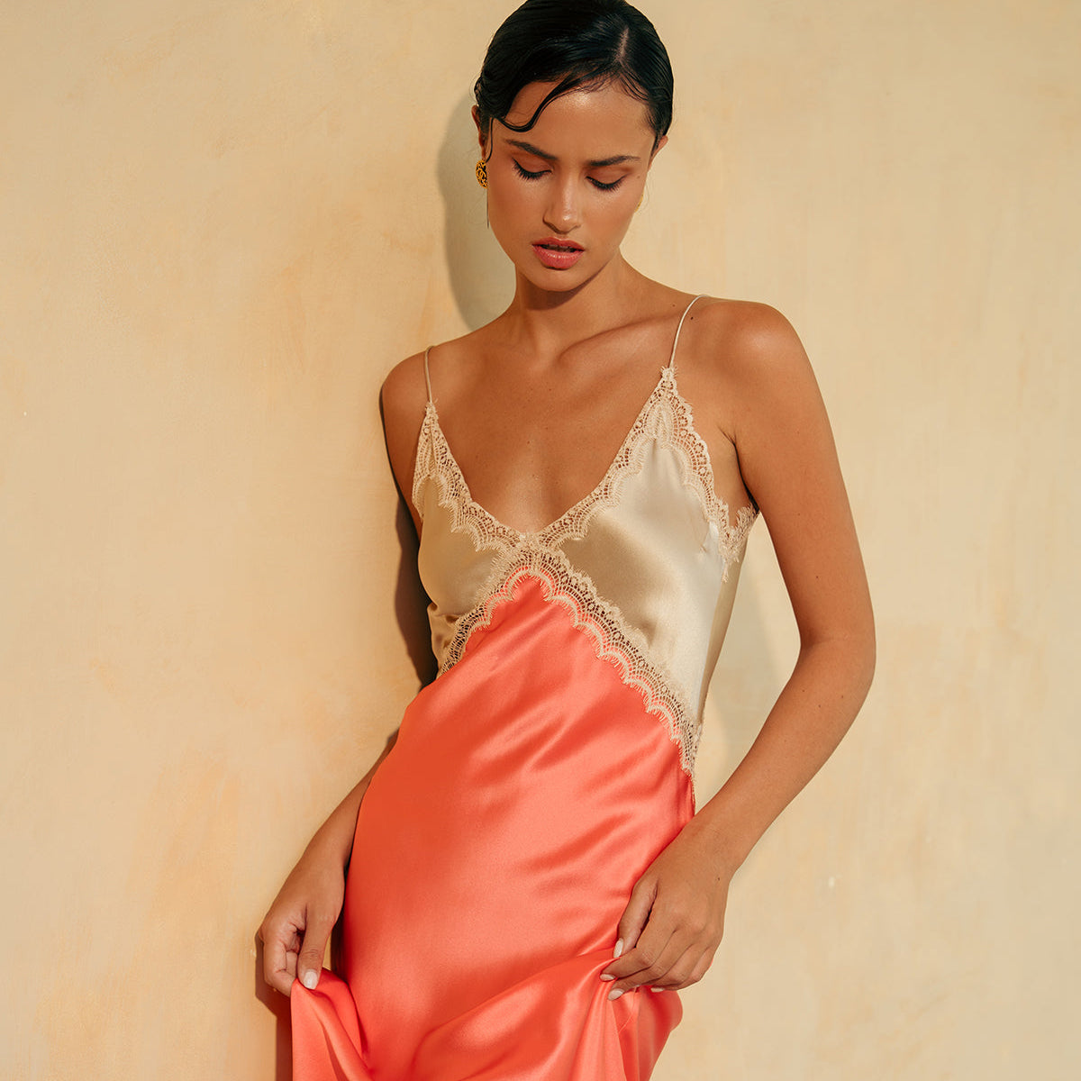 Woman wearing a satin slip dress with a gold lace top on a beige background