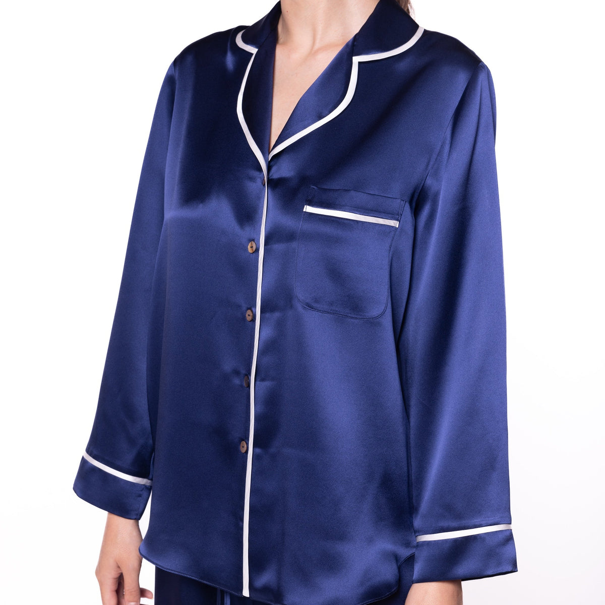 A woman wearing a navy blue satin pajama set with white piping trim, featuring a long-sleeve button-up top and matching pants, shown against a plain white background.