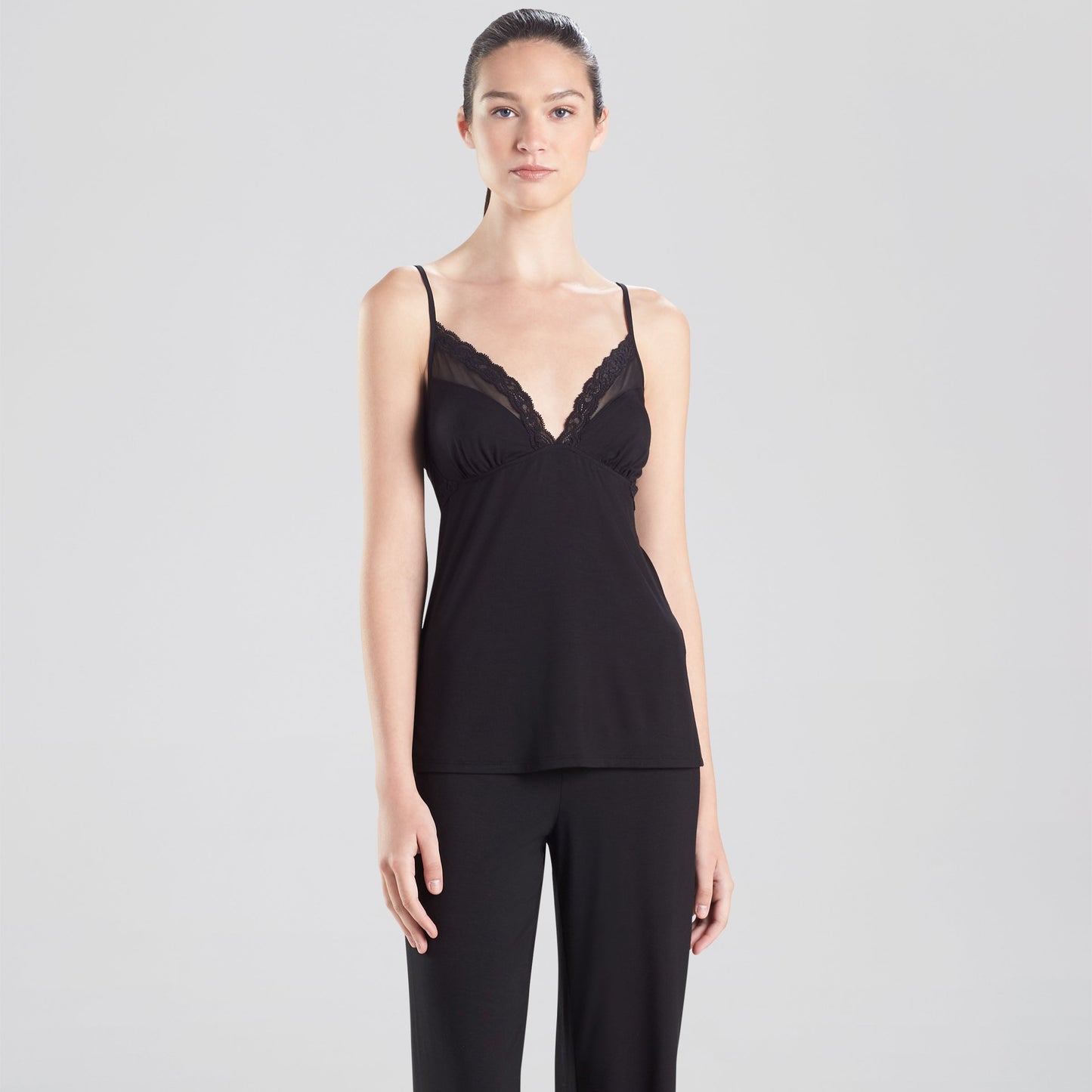 Woman wearing a black lace camisole and wide-leg pants on a white background