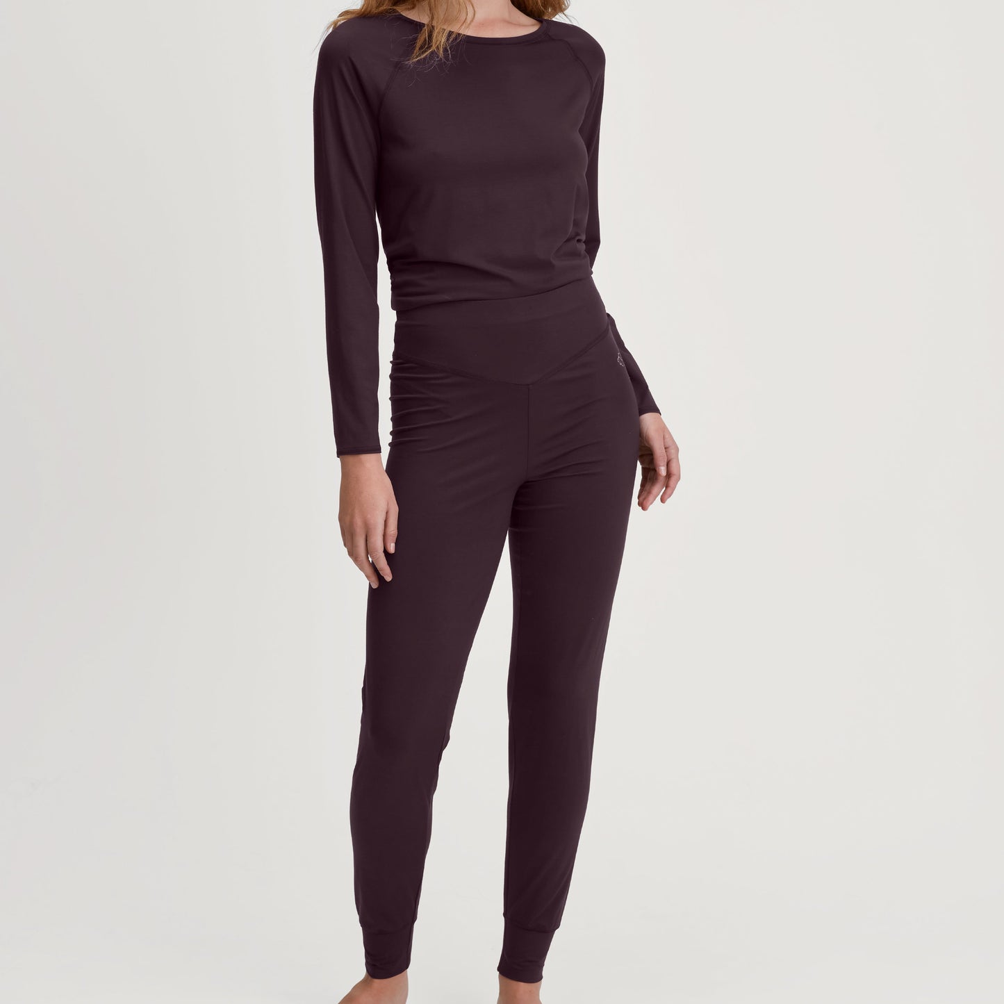 Woman wearing a dark purple long-sleeve top and leggings on a white background