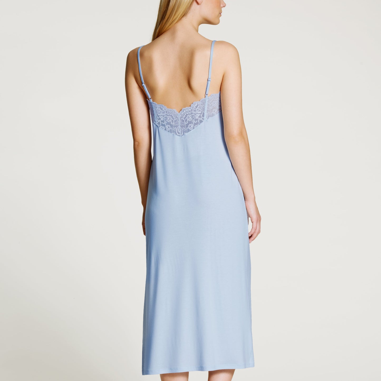 Woman wearing a light blue slip dress with lace details on a plain background
