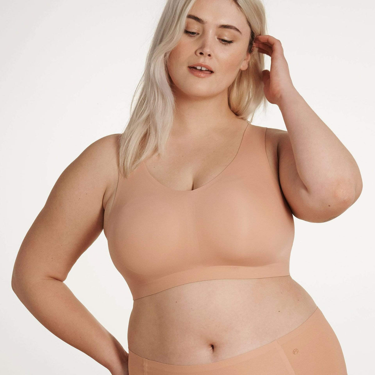 A woman wearing a beige, wireless, full-coverage pull-over bra.