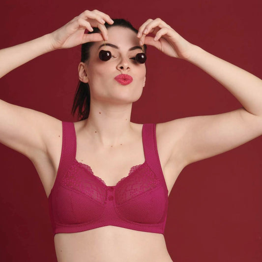 A woman wearing a cherry red, wirelessly supported, knitted fabric bra with French polka dot charm, posing with one hand raised to her head.