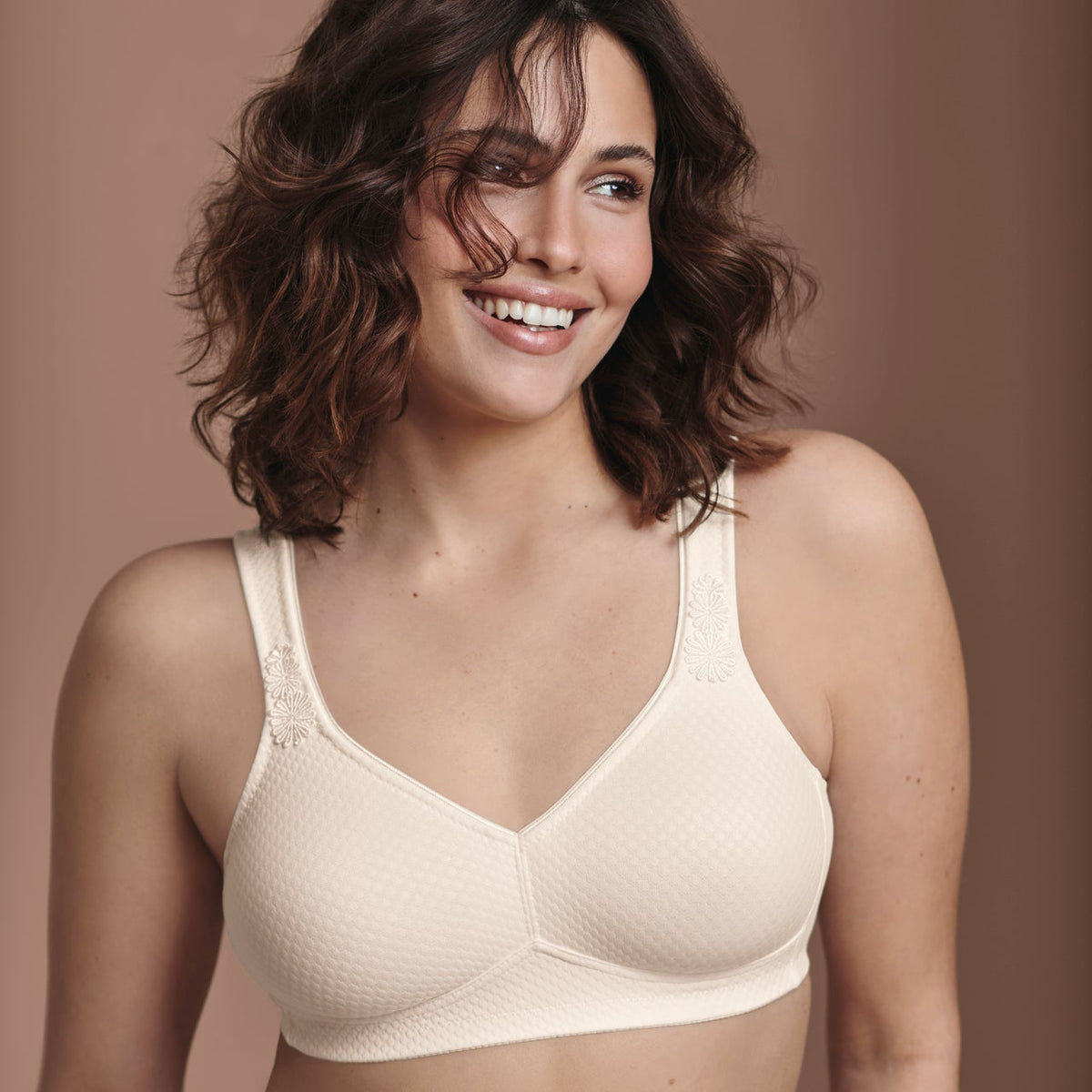 Woman wearing a beige bra and panties set against a brown background