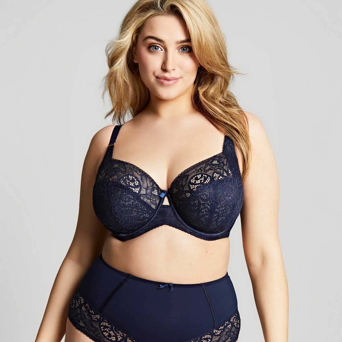 Woman wearing a navy blue lace bra and panties set on a plain background