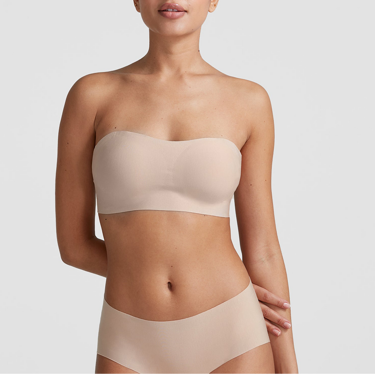 Woman wearing a beige strapless top and underwear set on a light gray background