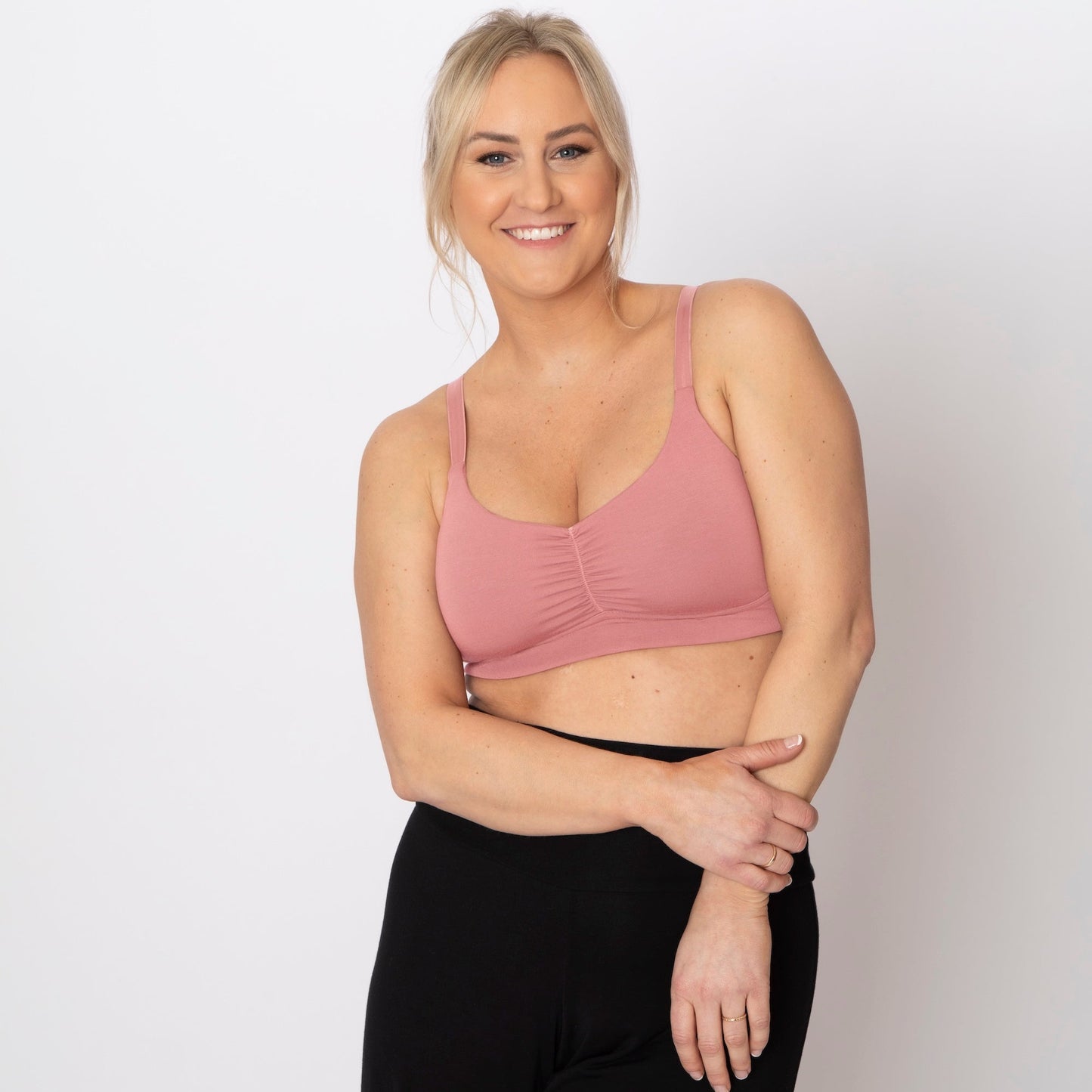 Woman wearing a pink sports bra and black leggings on a white background
