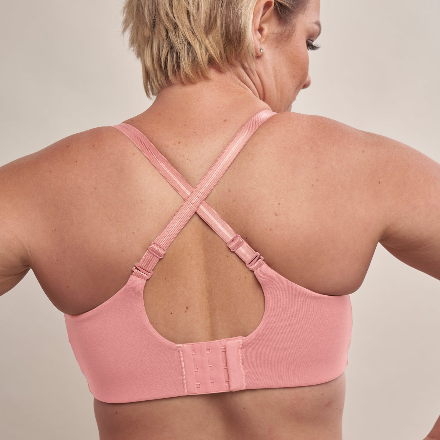 Person wearing a pink sports bra with criss-cross straps on a neutral background