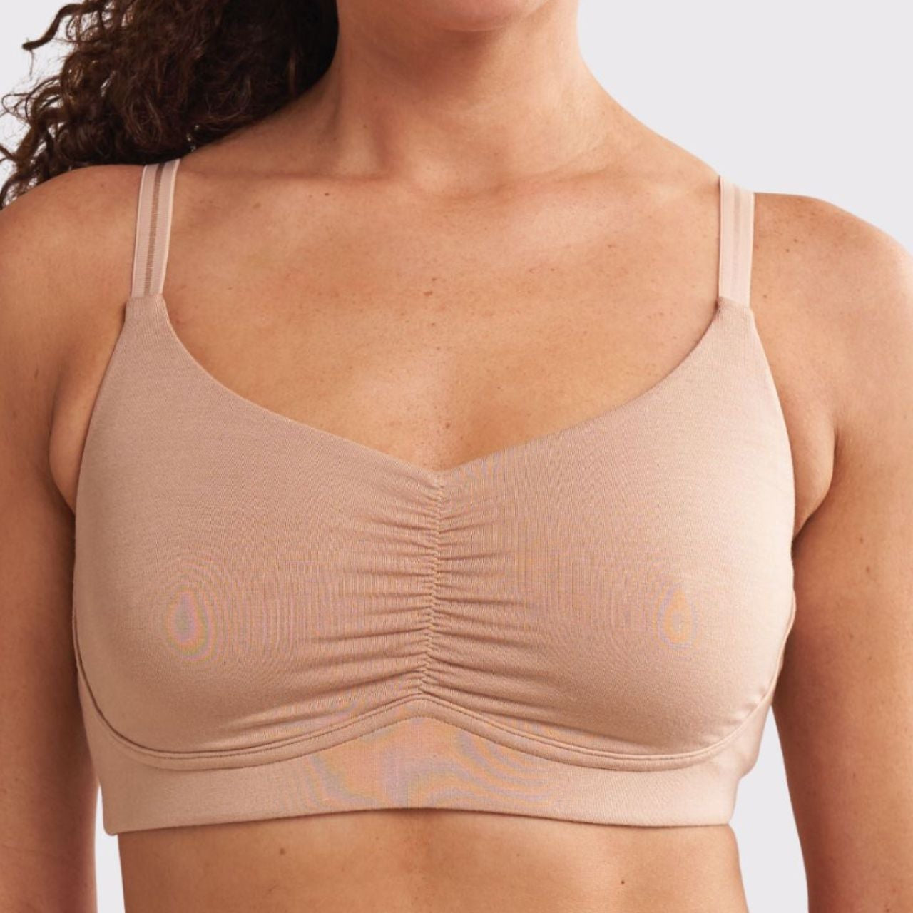 A woman wearing a beige, full coverage, wire-free bra with a ruched front.