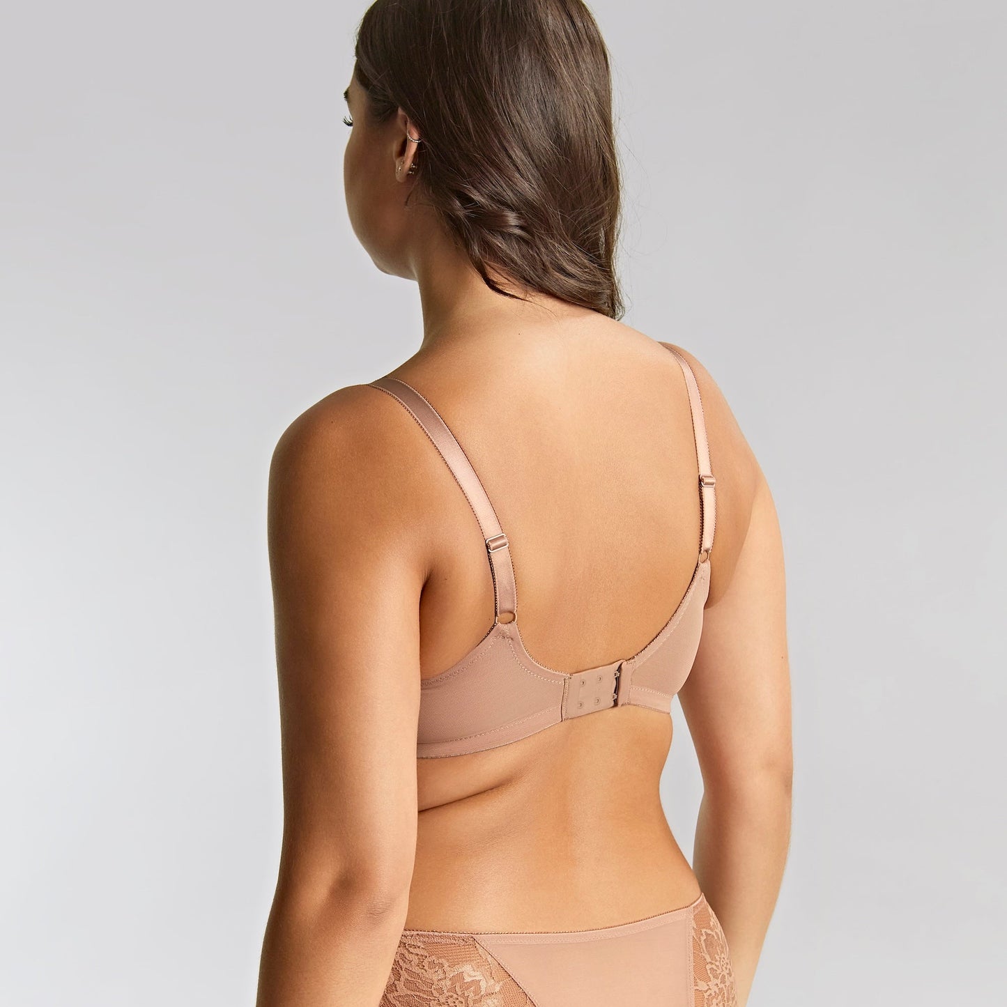 Woman wearing a beige lace lingerie set on a plain background