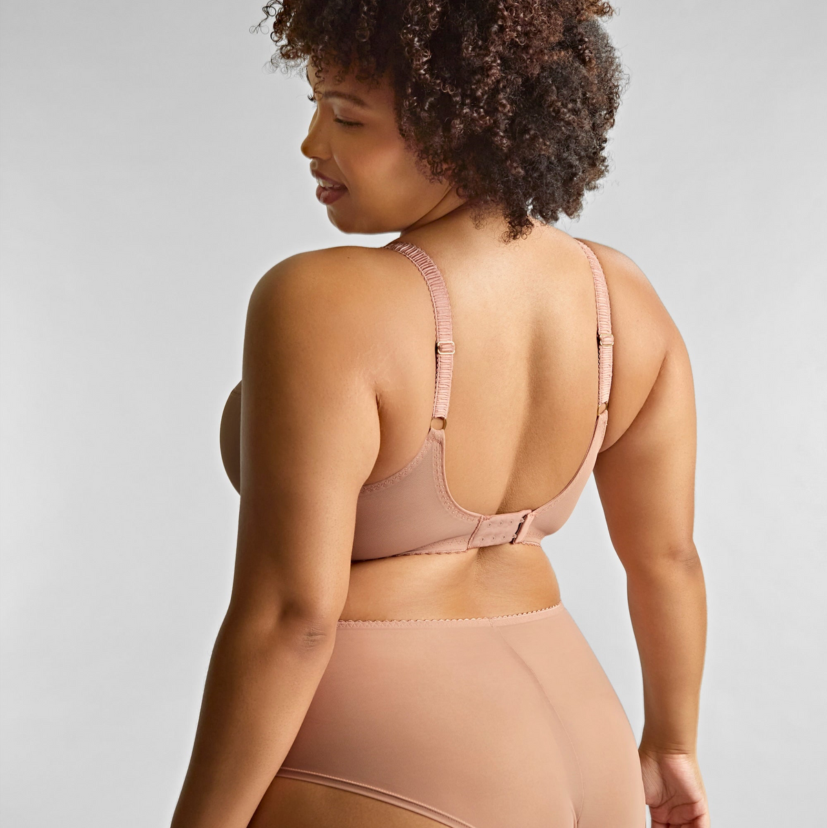 Woman wearing a beige bra and underwear set against a plain background