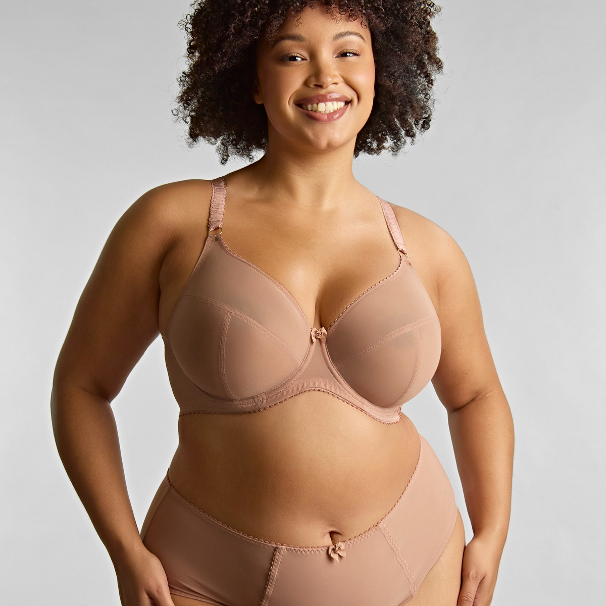 Woman wearing a beige bra and panties set on a plain background