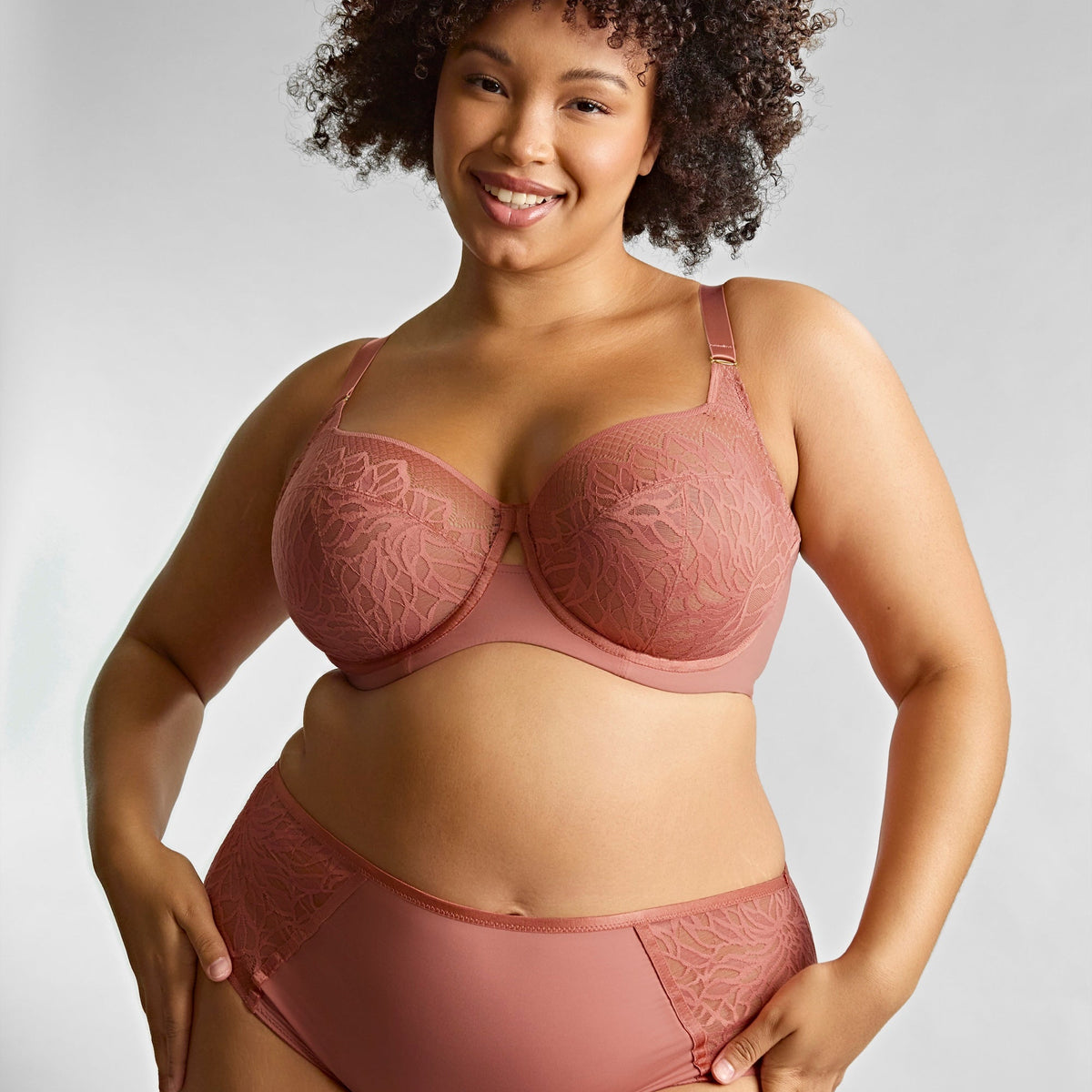Woman wearing a pink bra and panties set against a plain background