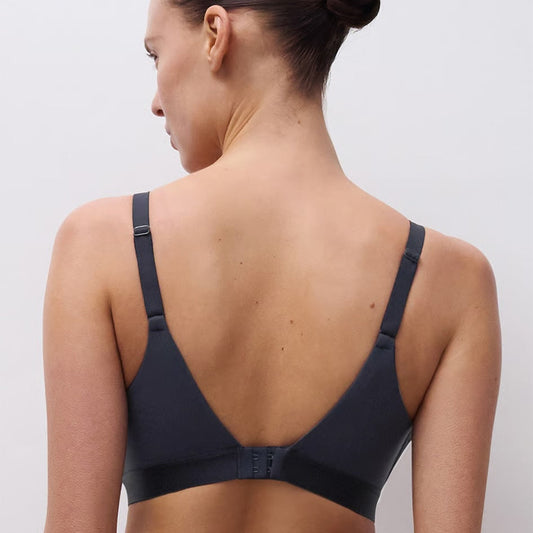 A woman shown from the back wearing a dark navy blue bra with a wide, open V-back design and adjustable shoulder straps, set against a plain light gray studio background.