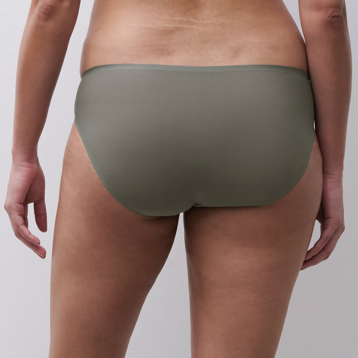 Rear view of a model wearing low-rise, solid olive green underwear against a light gray studio background.