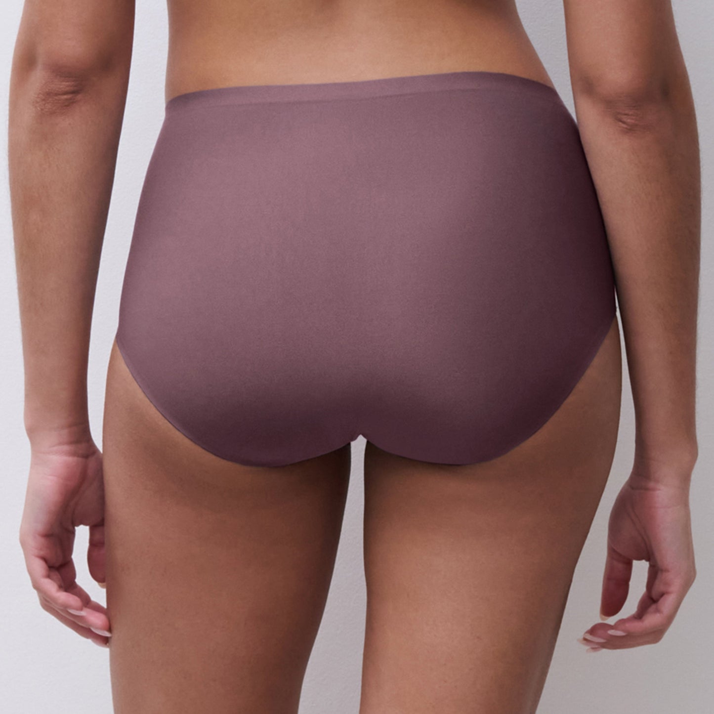 Rear view of a model wearing high-waisted, seamless underwear in a muted mauve-purple color, set against a plain light gray background.