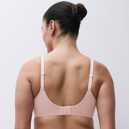 A woman shown from the back wearing a light pink bra and matching underwear against a plain light gray studio background.