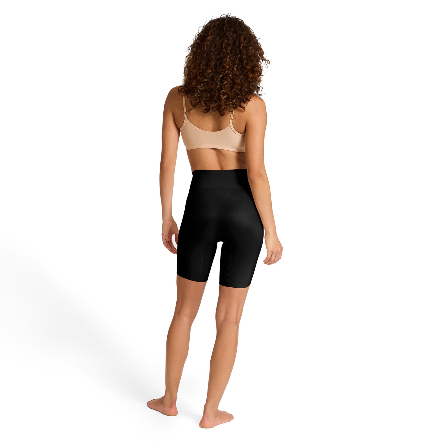 Person wearing a beige bra and black high-waisted shaper shorts on a white background