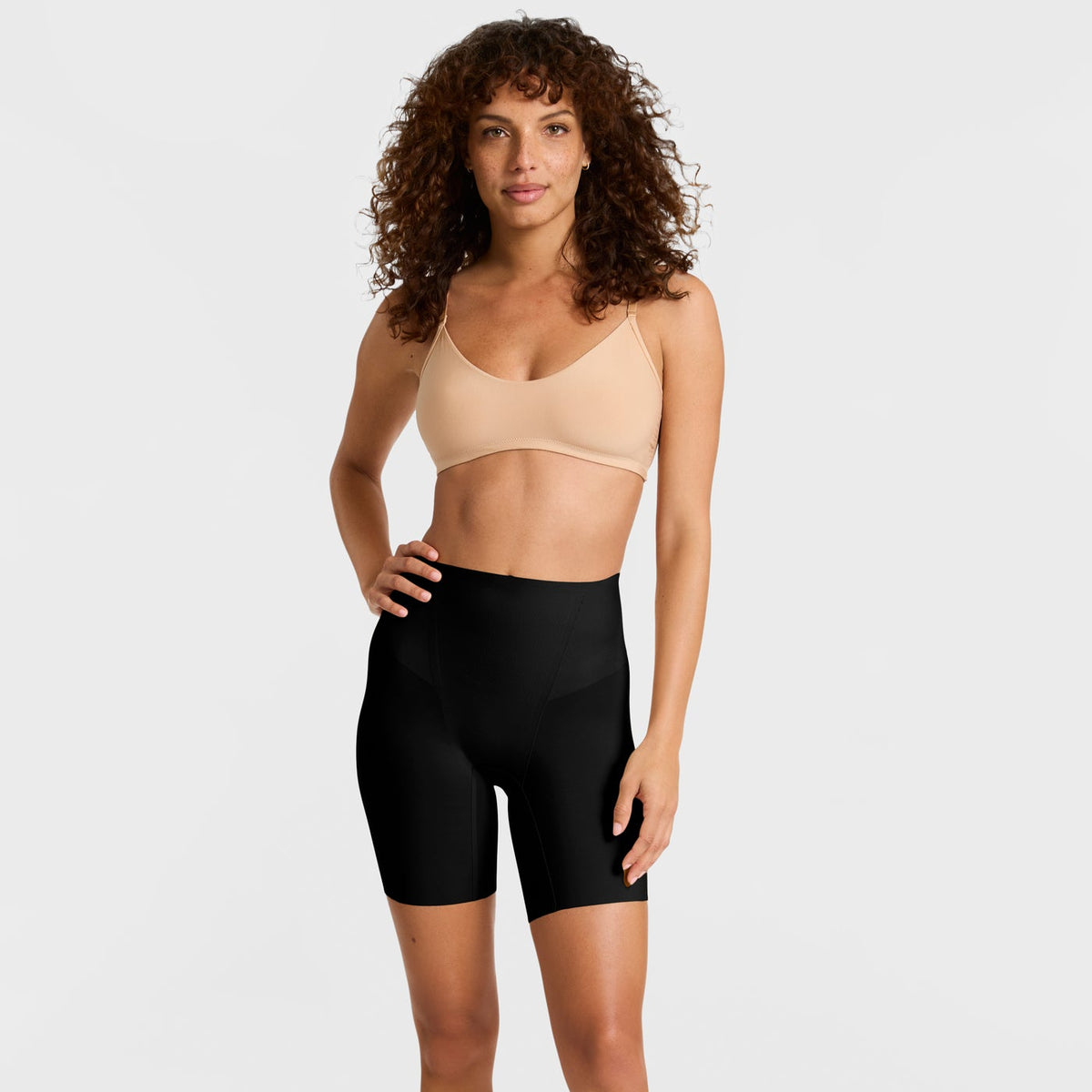 Woman wearing a beige bra and black shaper shorts on a white background