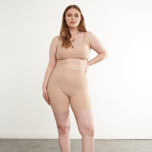 A person wearing beige zone smoothing shorts with a super-high rise and raw-cut hem, standing against a neutral background.