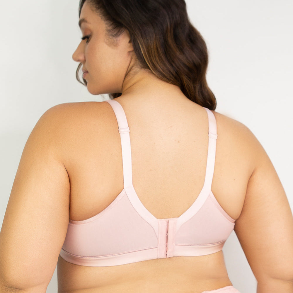 Woman wearing a light pink bralette against a plain background