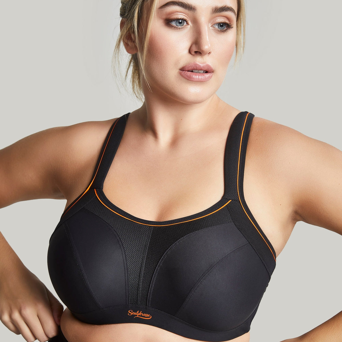 A woman wearing a black sports bra with orange detailing.
