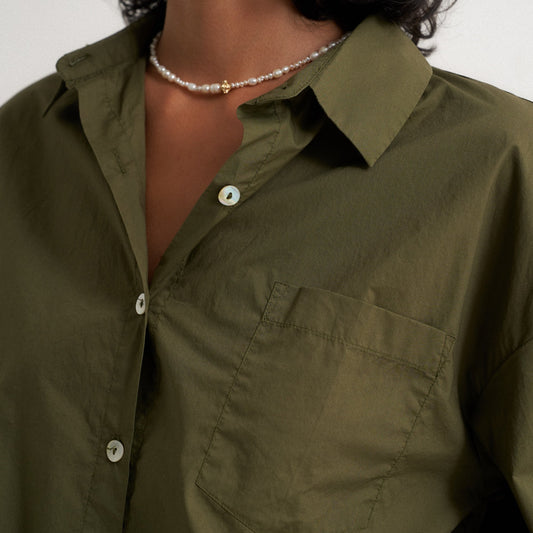 Person wearing a green shirt with a pearl necklace against a neutral background