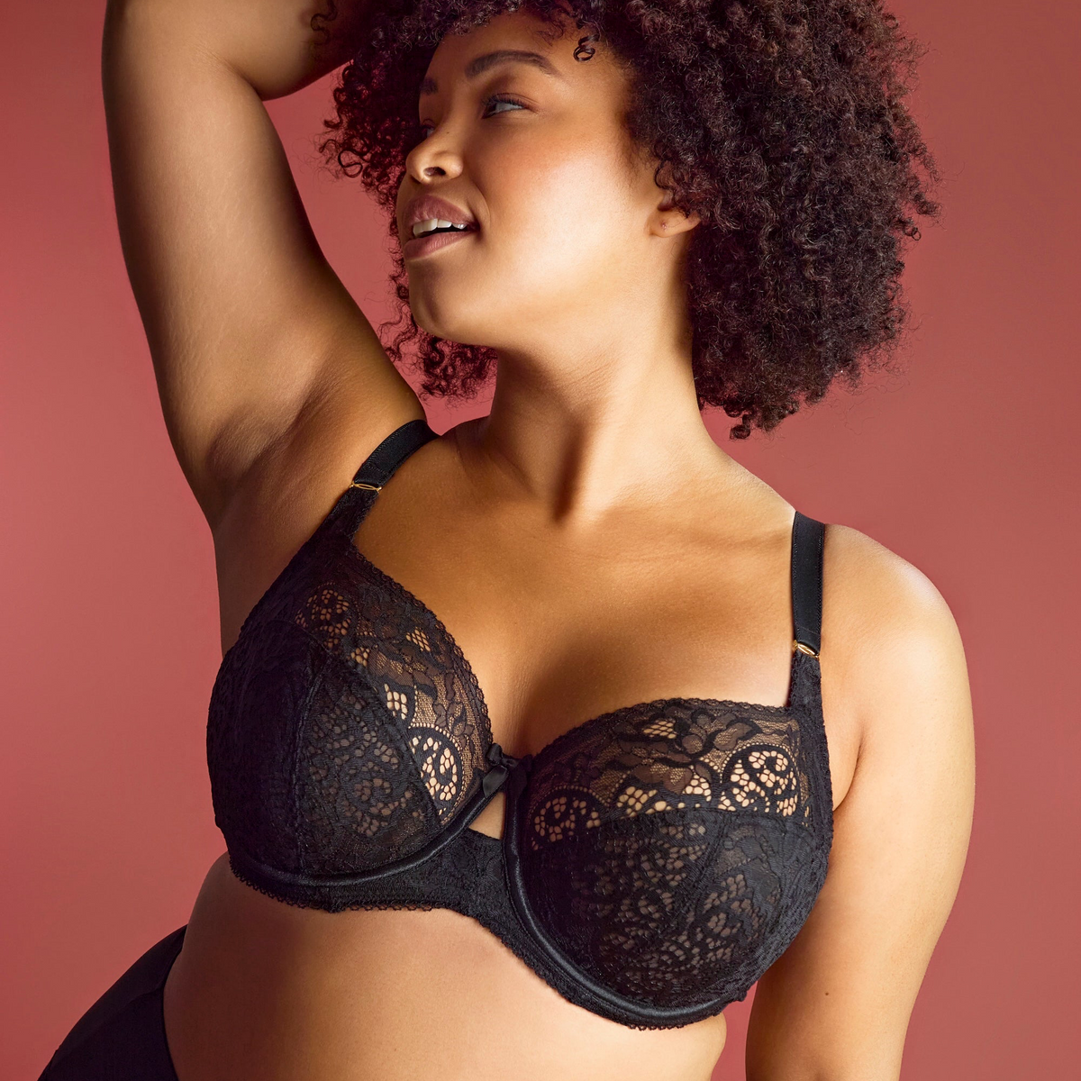 Woman wearing a black lace bra against a pink background