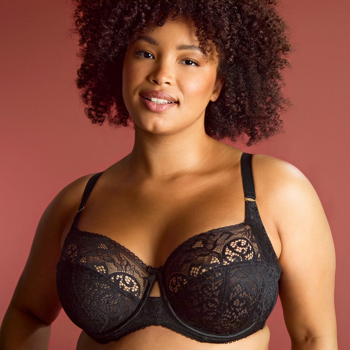Woman wearing a black lace bra against a pink background