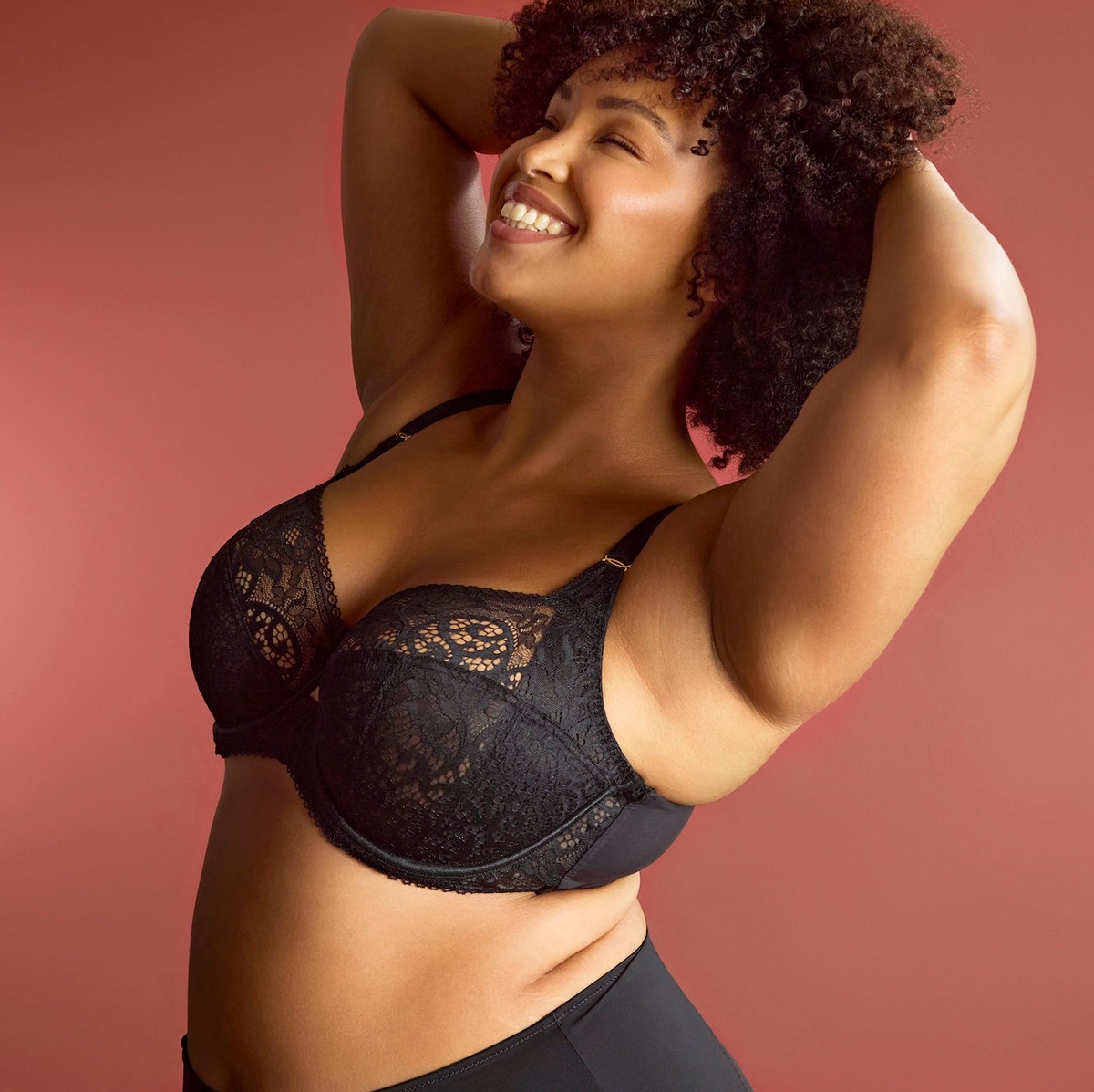 Woman wearing a black lace bra against a pink background