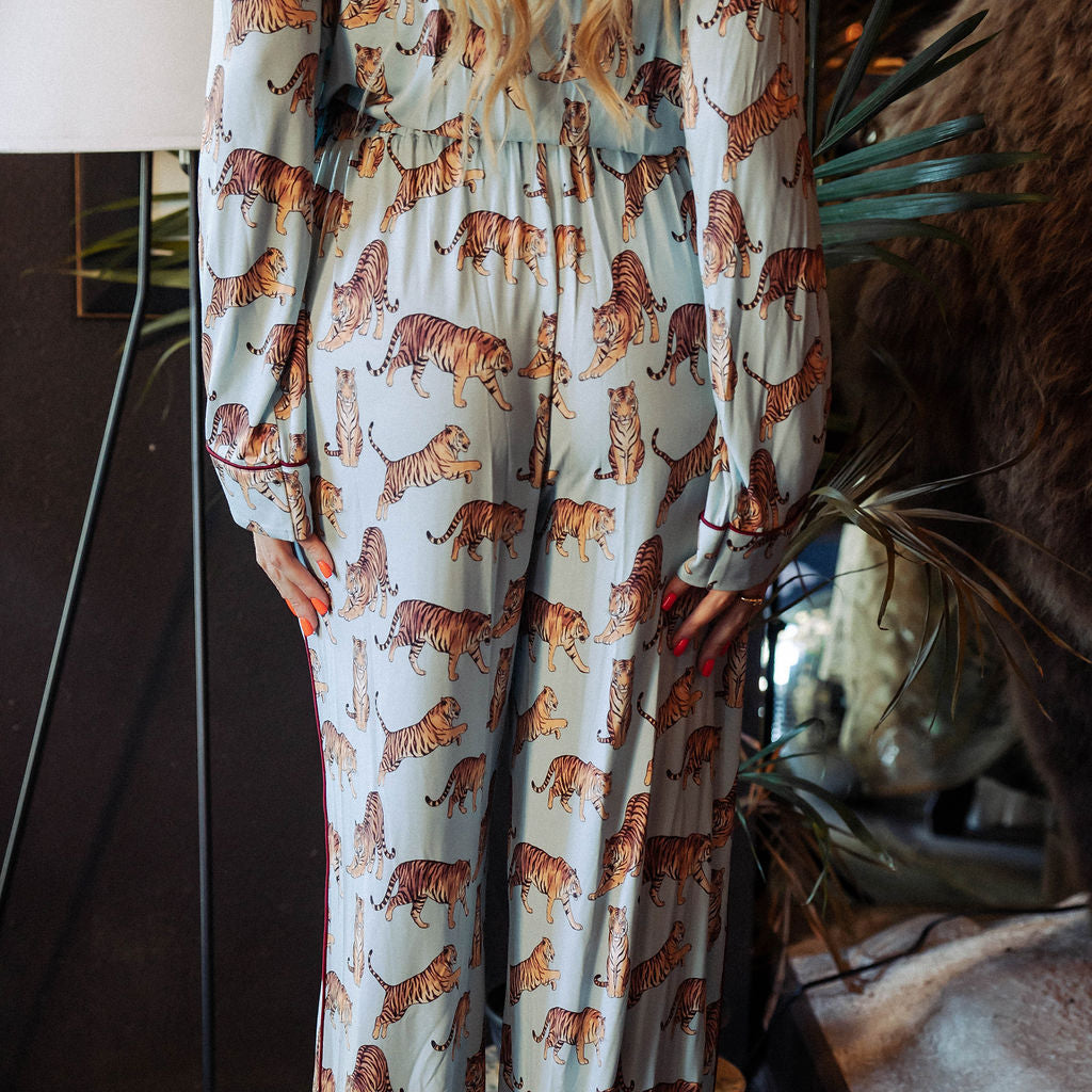 A long-sleeve maxi dress with an allover tiger print on a light blue-gray background, worn by a model in an indoor styled setting.