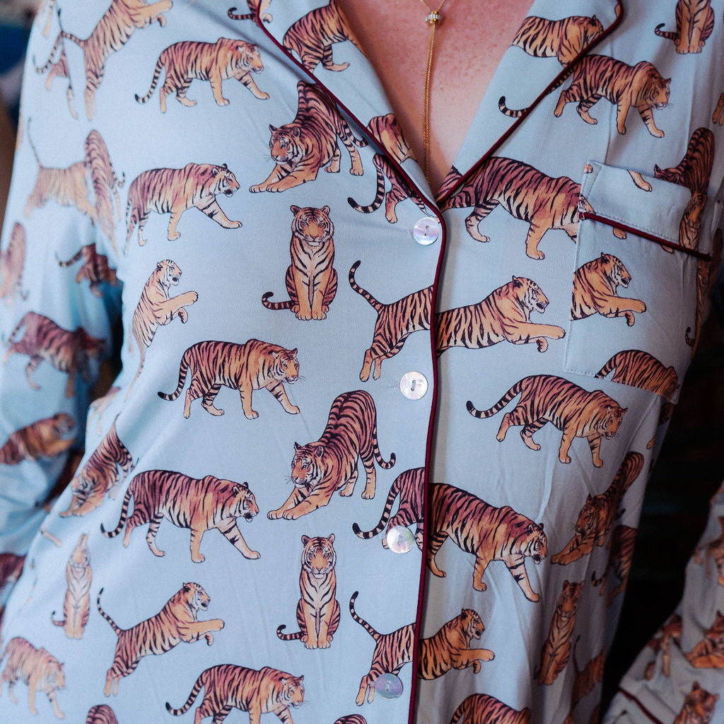A close-up of a person wearing a pajama-style button-front shirt with an allover tiger print. The fabric is a pale blue-gray, and the repeating pattern shows tigers in orange, brown, black, and cream.