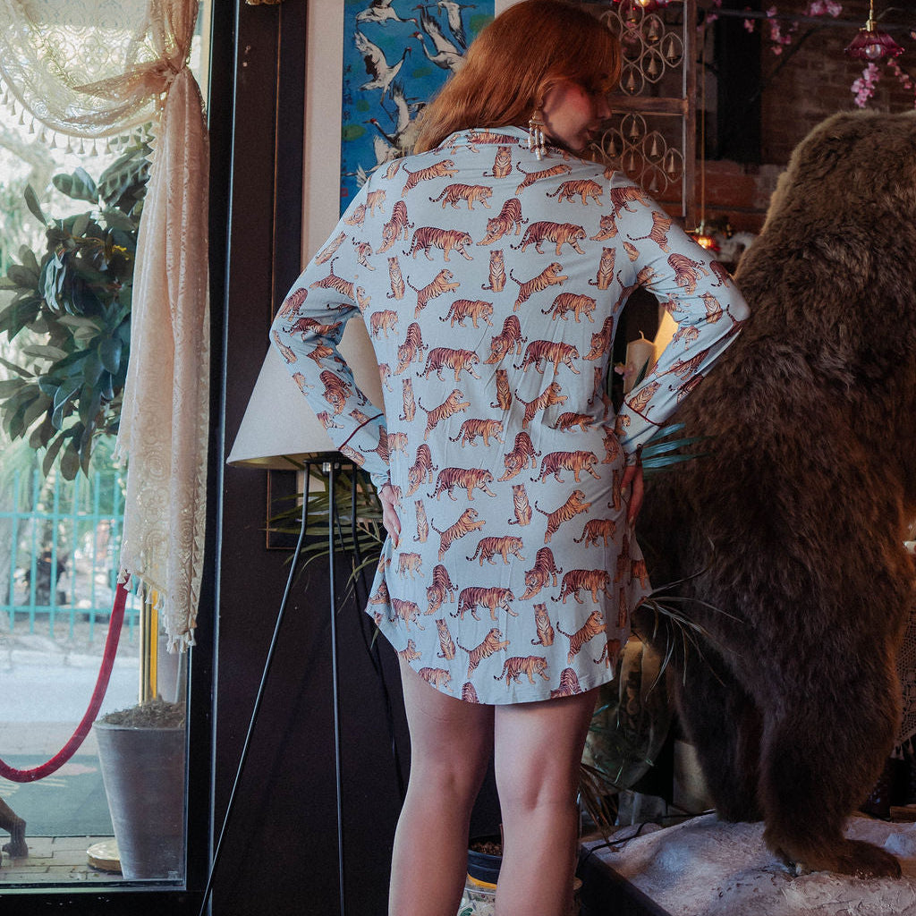 A person stands with their back to the camera wearing a long-sleeve pajama shirt with an all-over print of cartoon animals on a light background. The setting appears to be a vintage or antique shop interior with a taxidermy bear and framed art in the background.
