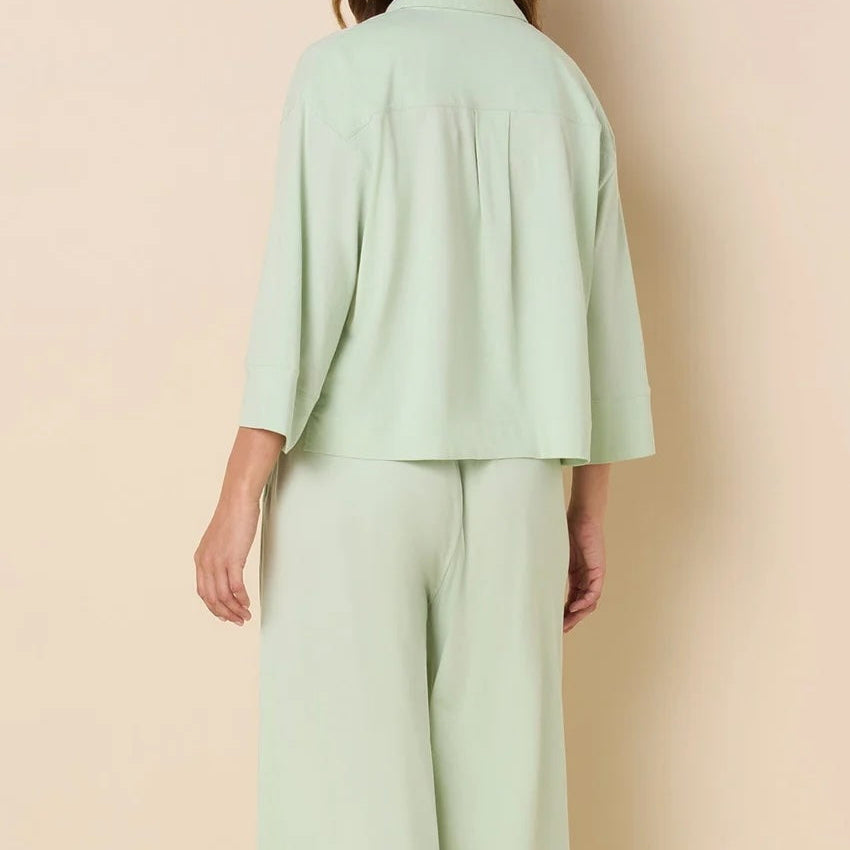 Woman wearing a light green outfit with wide-leg pants against a beige background