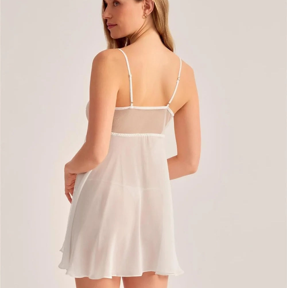 A woman wearing a white sheer slip dress with thin straps, shown from the back against a plain light gray studio background.