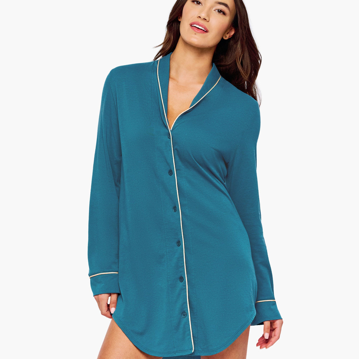 A woman modeling a teal long-sleeve button-front shirt dress with thin cream piping details on the collar, front placket, and cuffs, set against a plain white studio background.
