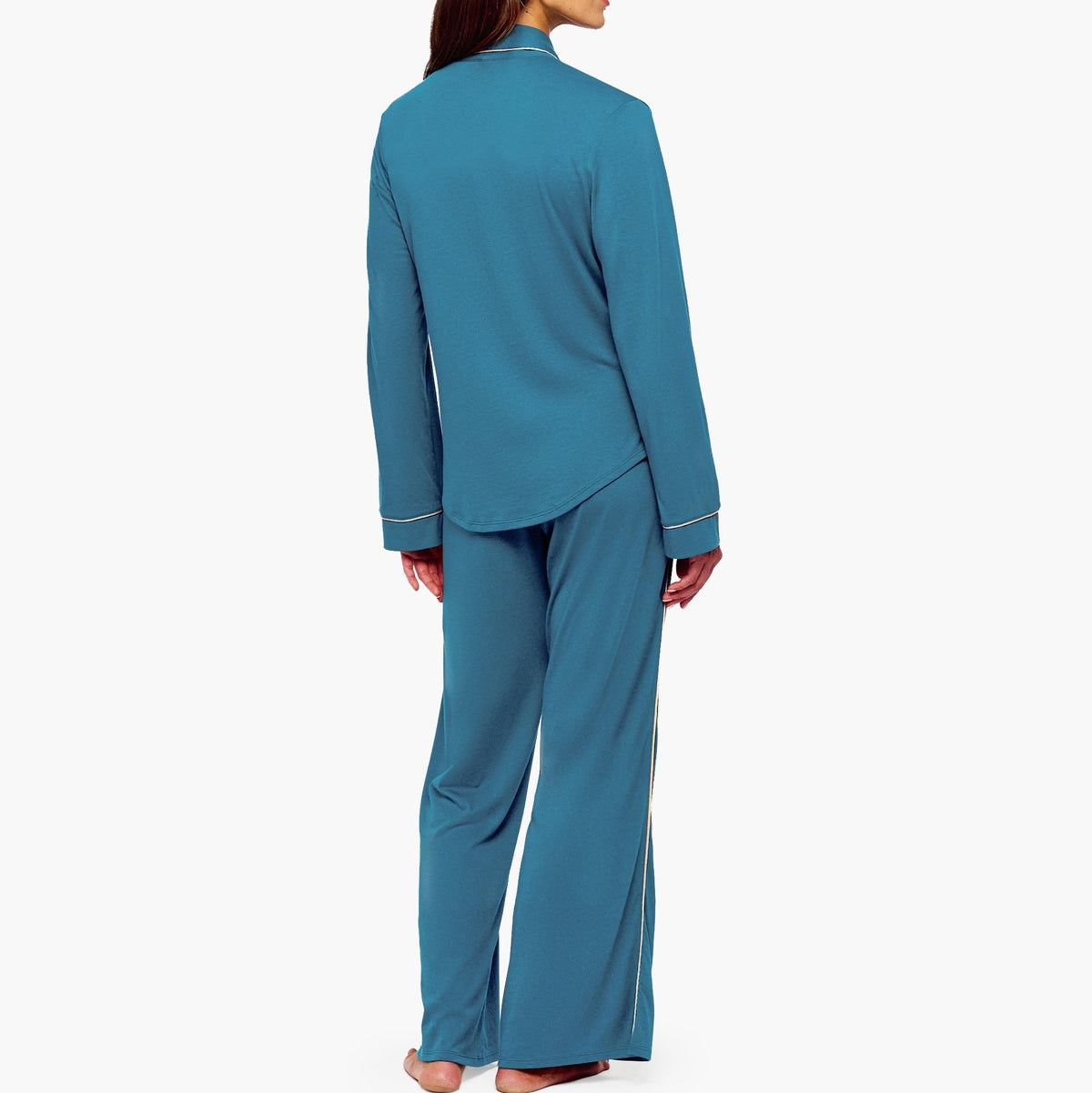 A woman shown from the back wearing a matching teal blue pajama set with a long-sleeve top and wide-leg pants, photographed against a plain light gray studio background.