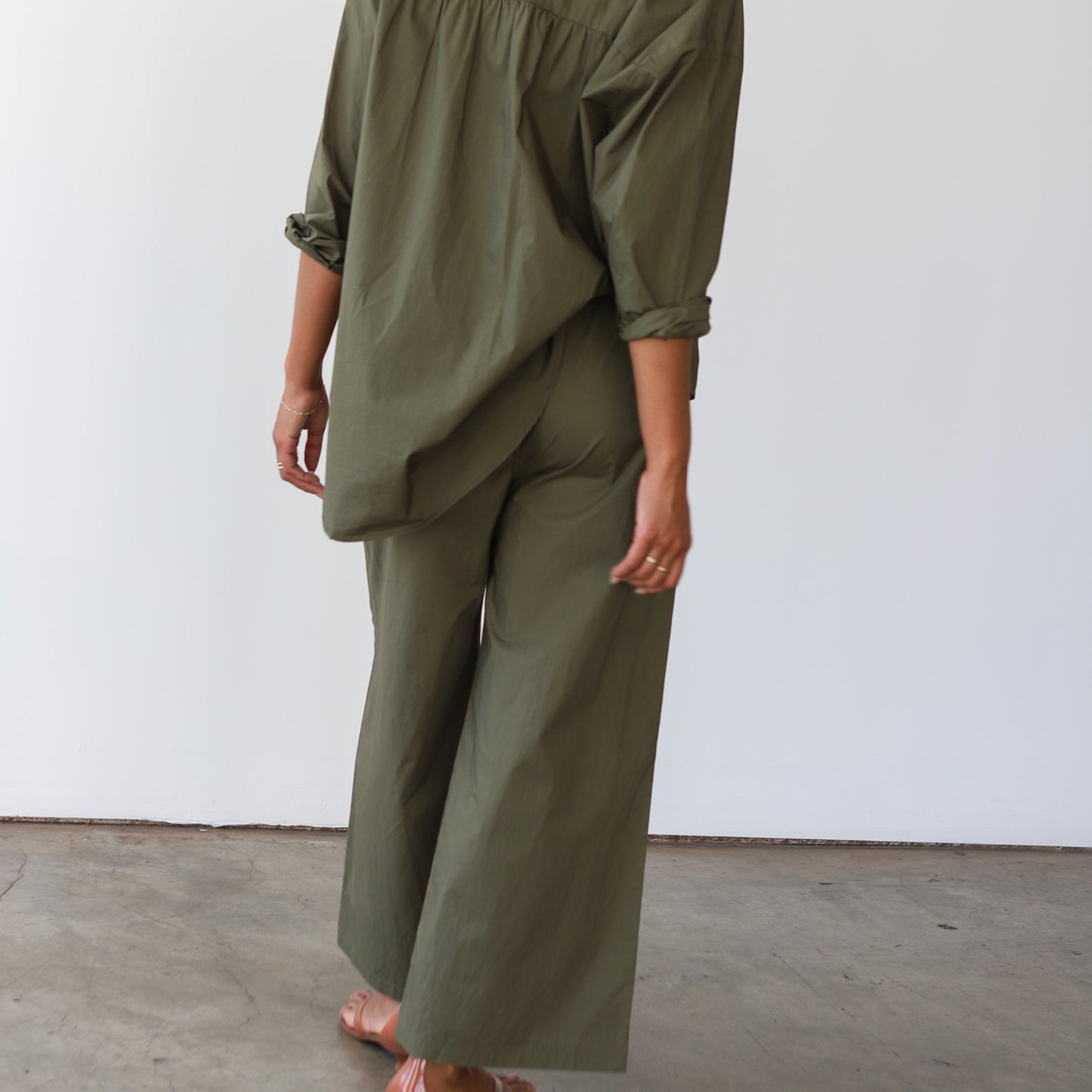 Person wearing a green outfit standing against a white wall.