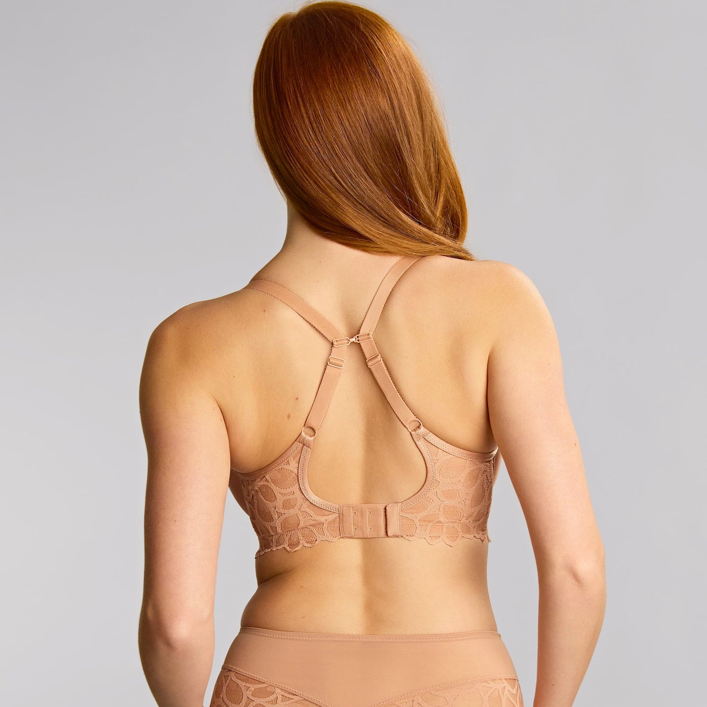 Woman wearing a beige lace lingerie set on a plain background