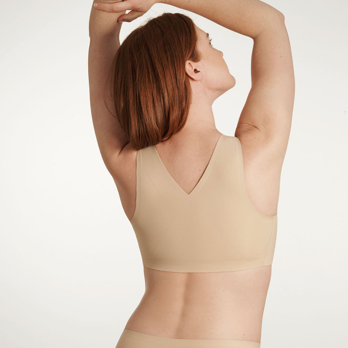 Woman wearing a beige bralette against a white background
