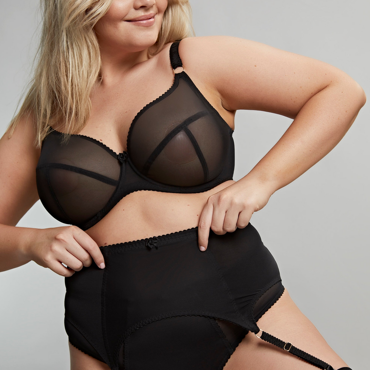 Woman wearing a black sheer bra and panties set against a gray background