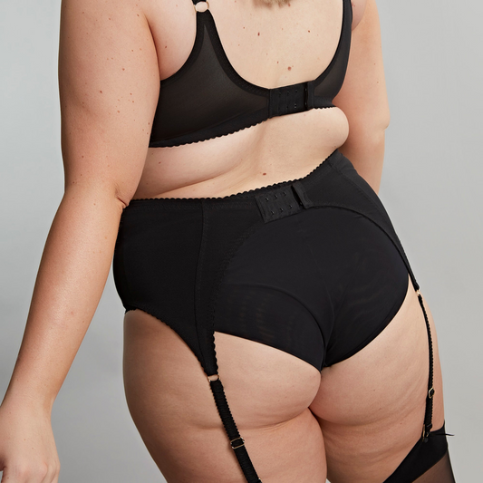 Person wearing black high-waisted underwear with suspenders on a plain background