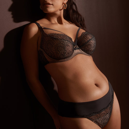 A woman wearing a flirty tulle thong with floral embroidery and a black edgy tattoo effect.