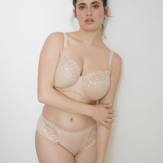 Woman wearing a beige lace lingerie set against a plain background
