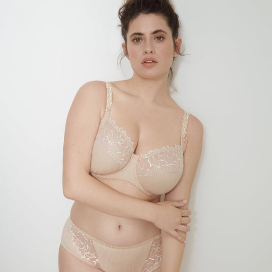 Woman wearing a beige lace bra and panties set against a plain background