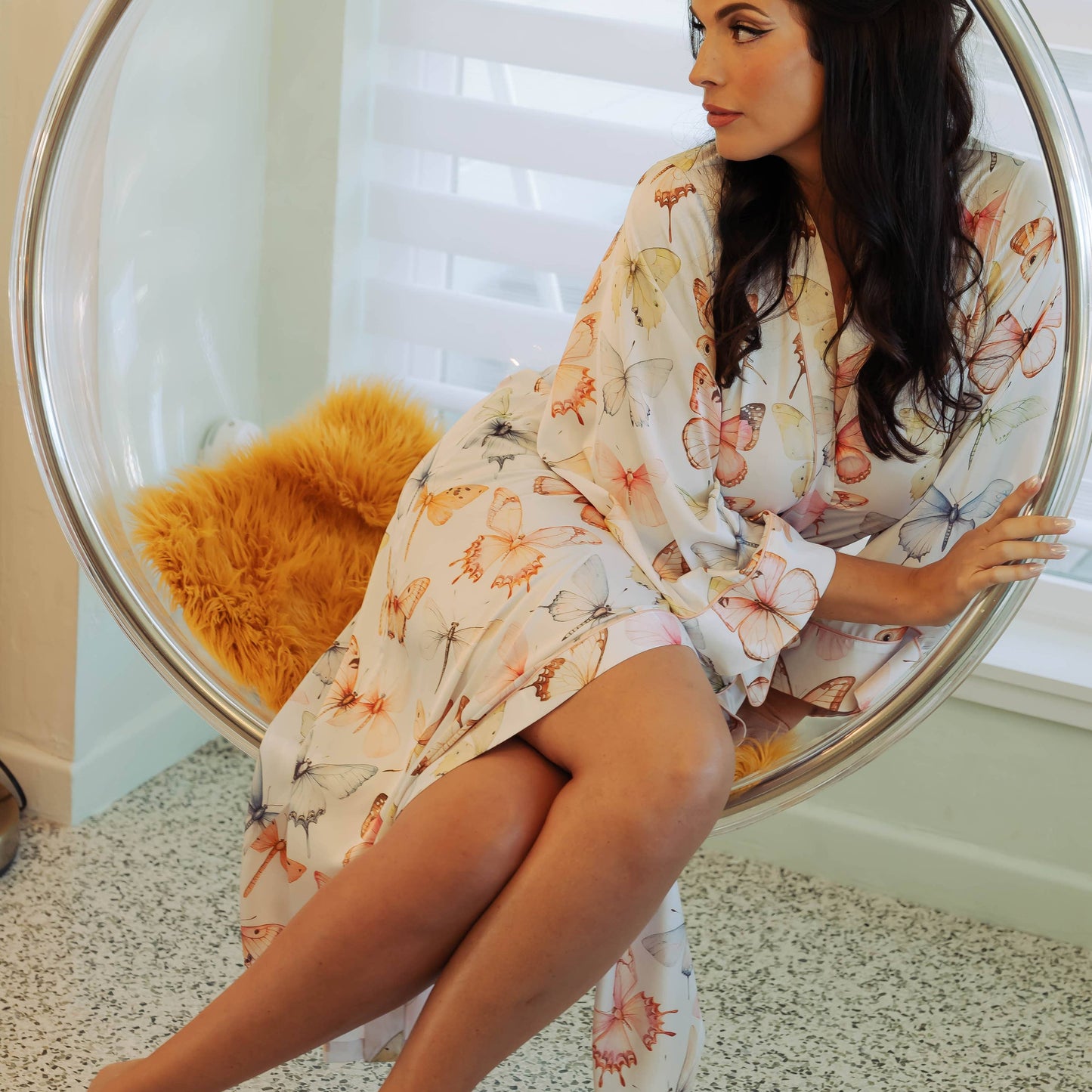 Woman in a floral dress sitting in a round chair with a white background